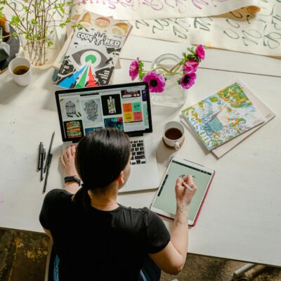 Photo of Woman Writing on Tablet Computer While Using Laptop